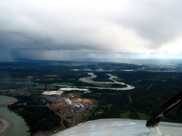 Aerial view of a large pulp mill with steam plumes on the edge of Prince George