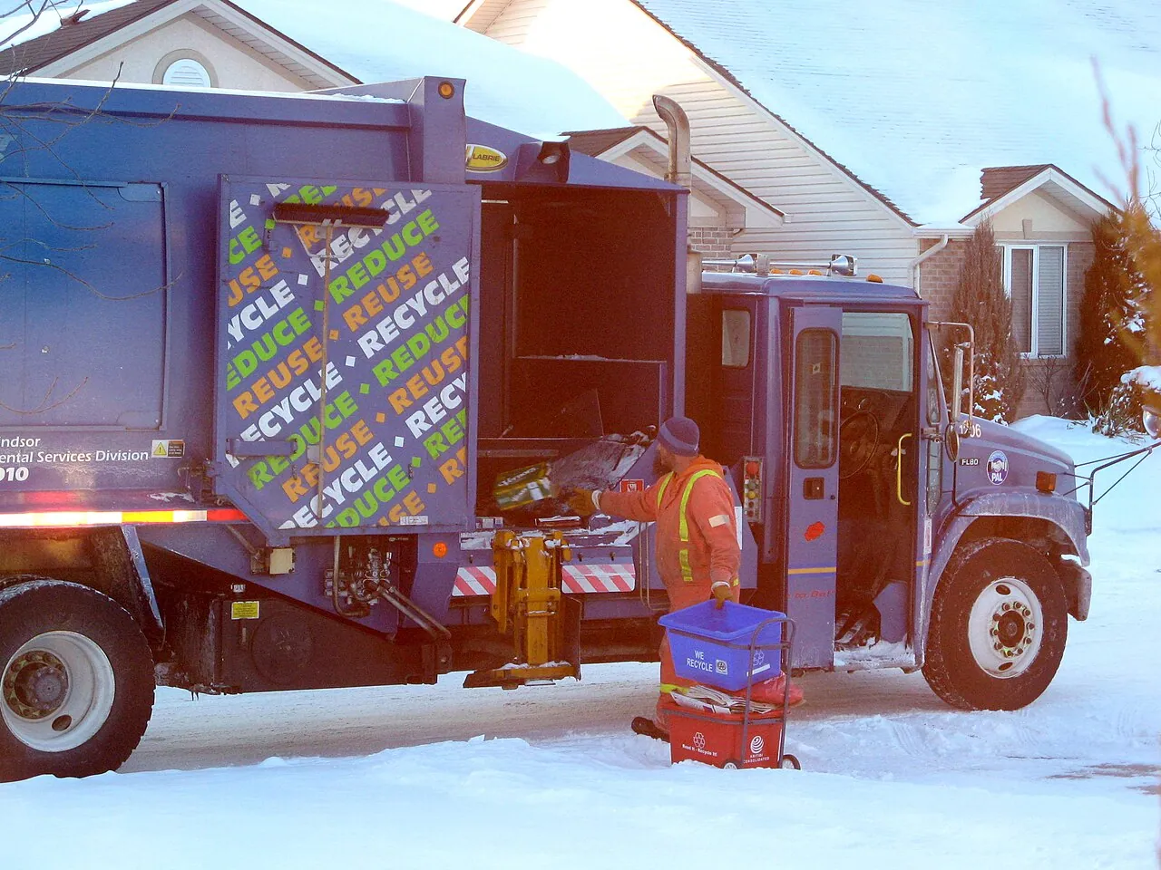 A curbside recycling truck collecting on a snowy residential street in winter (a truck in Leamington, Ontario, shown as a generic example)