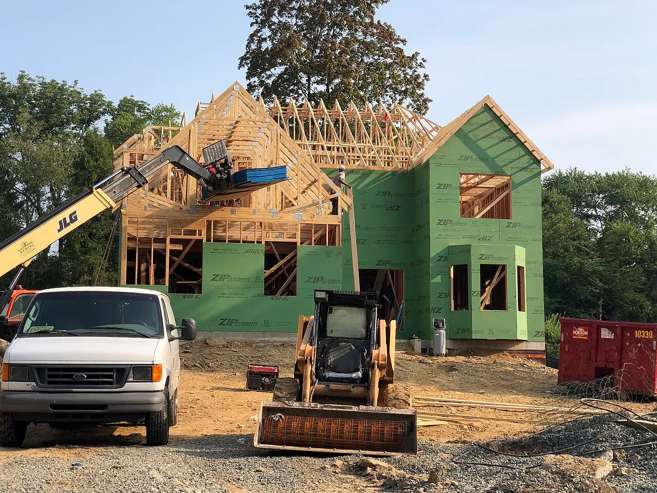 A new wood-frame house under construction with a lift and a skid steer on the lot (a generic example photographed in New Jersey)
