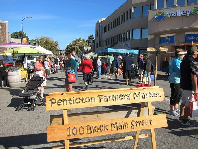 Shoppers browsing stalls at a busy outdoor farmers’ market (Penticton, shown as a generic example of a BC market)