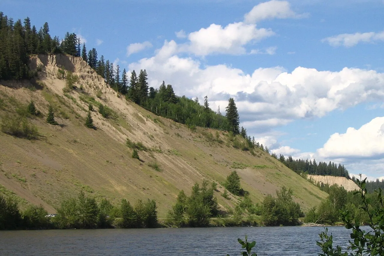 Tall pale silt cliffs rising above the Nechako River under a blue sky