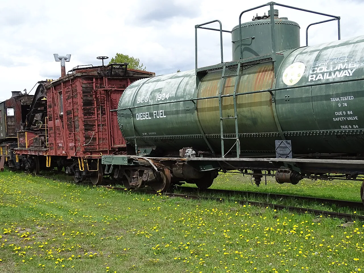 A vintage wooden boxcar and tank car on display on the grass at the railway and forestry museum