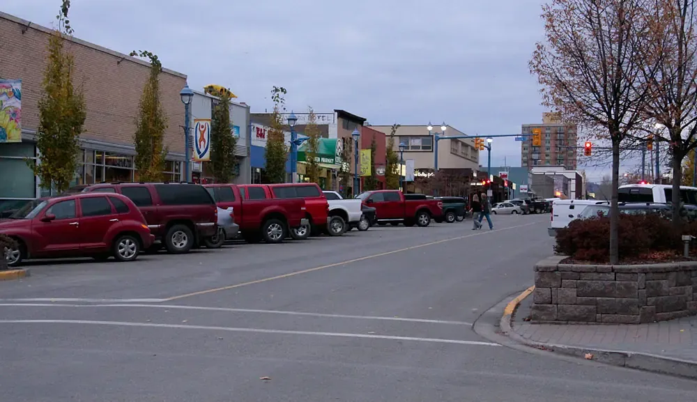 Pickup trucks parked in front of a row of shops on a Prince George street in autumn