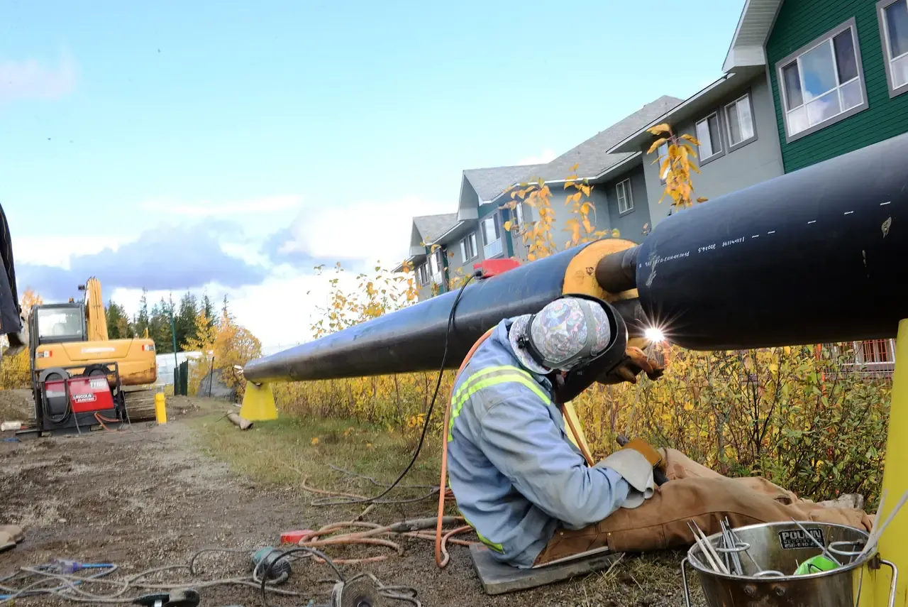 A welder in safety gear welding a large pipe on the UNBC campus in Prince George